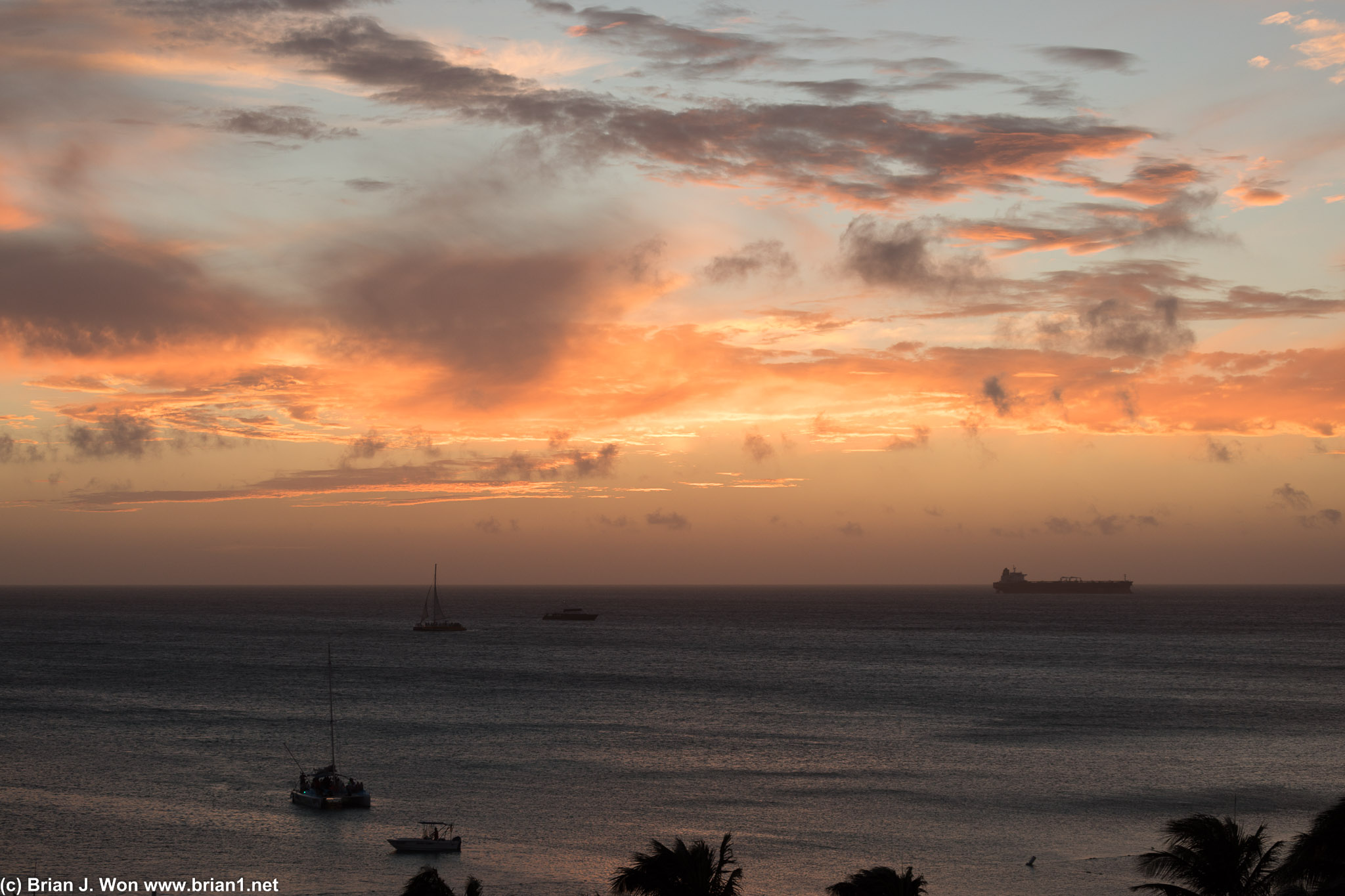 Sailboats, snorkel boats, and a single cargo ship take in the sunset.