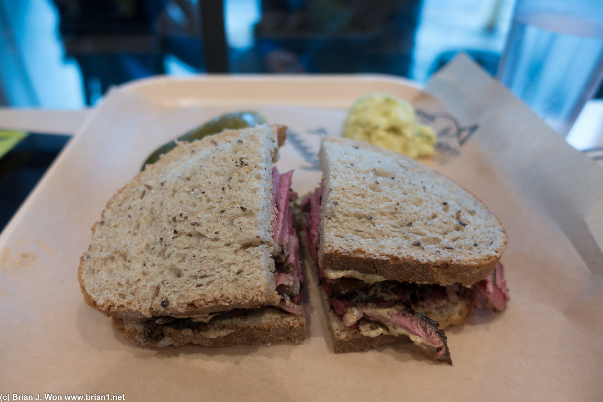 Pastrami sandwich with potato salad and pickle.