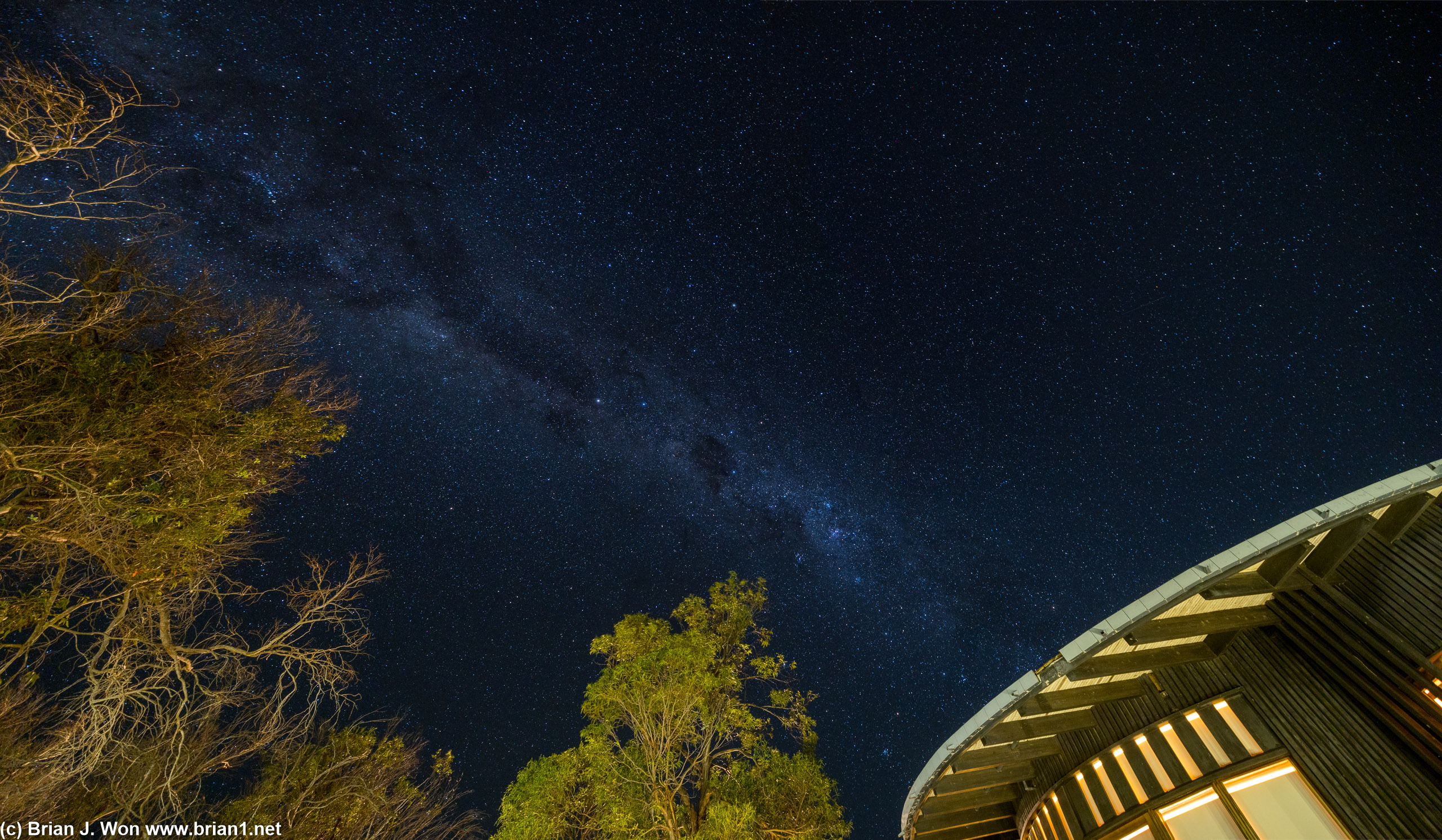 The galactic center visible over lights and trees of the hotel.