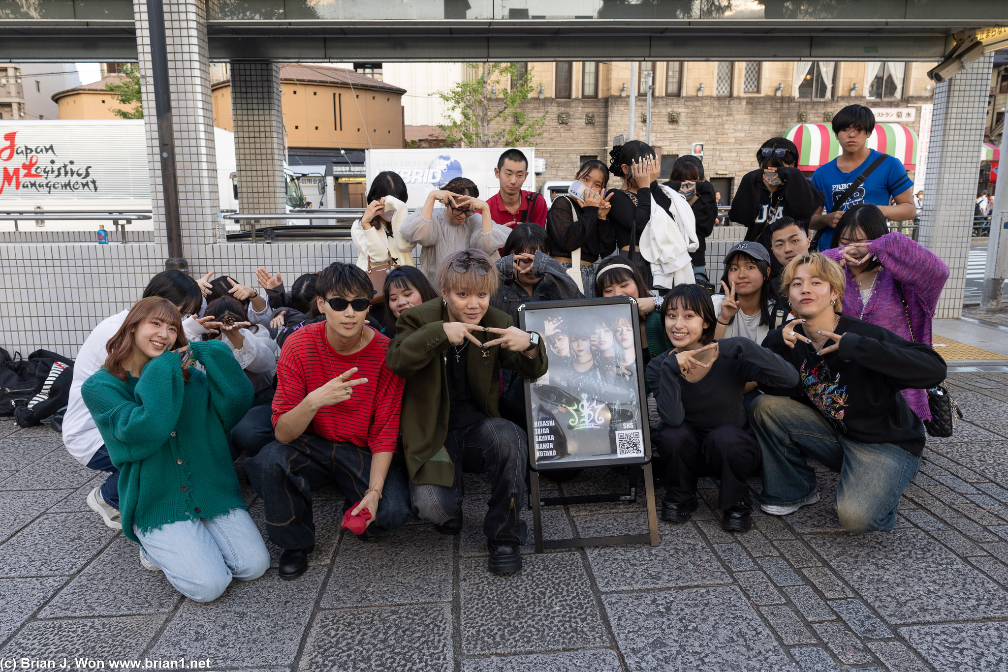 I$M J-pop band with a crowd of fans (and two clueless American tourists) taking pictures.